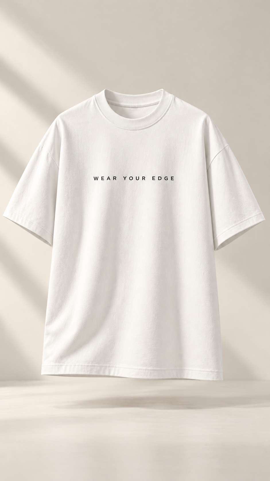 A white short-sleeve crewneck t-shirt with the text 'WEAR YOUR EDGE' printed in black across the chest, displayed against a warm beige background with soft diagonal shadows.